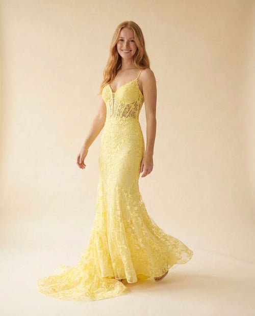 Femme portant une robe de bal sirène jaune en dentelle florale, avec bustier corseté, décolleté cœur, bretelles fines et longue traîne.