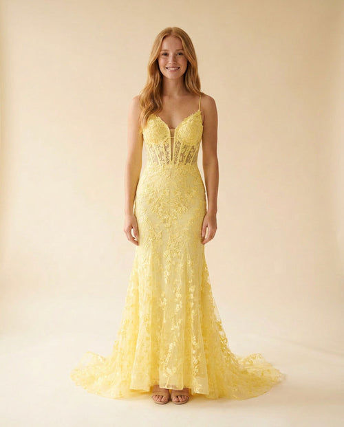 Femme portant une robe de bal sirène jaune en dentelle florale, avec bustier corseté, décolleté cœur, bretelles fines et longue traîne.