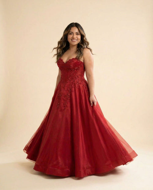 Femme portant une robe de bal rouge à bustier décolleté cœur, dentelle perlée et jupe de satin ample, vue de face.