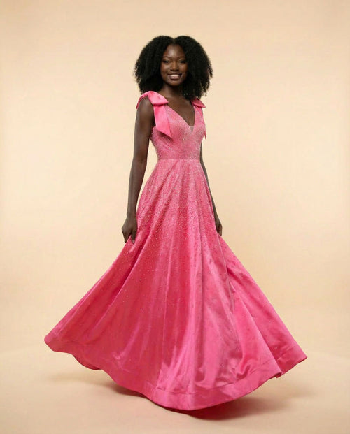 Femme portant une robe de bal rose flamboyant à boucles aux épaules, décolleté en V, bustier scintillant et jupe ample avec traîne.