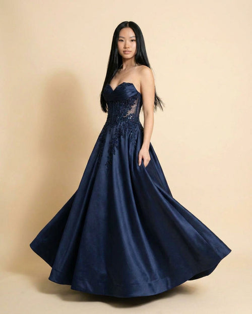 Femme portant une robe de bal marine à corsage transparent en dentelle perlée, encolure cœur et jupe princesse ample.