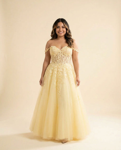 Femme portant une robe de bal jaune pâle à bustier corset transparent brodé de feuillage, décolleté cœur, épaules dénudées et jupe de tulle princesse volumineuse.