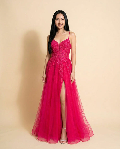 Femme portant une robe de bal magenta évasée en tulle, bustier de dentelle scintillante à décolleté cœur, fines bretelles et fente haute, vue de face.