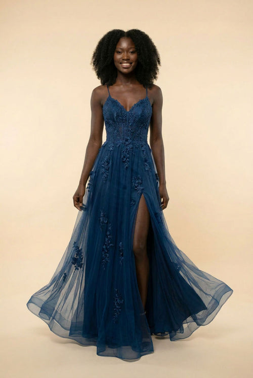 Femme portant une robe de bal évasée en tulle marine, bustier en dentelle, décolleté cœur et fente haute, devant un décor méditerranéen.