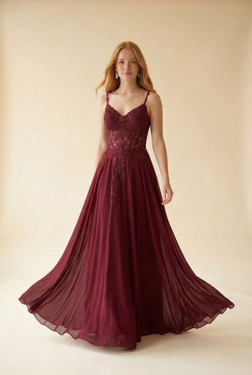Femme portant une robe de bal évasée bourgogne à bustier en dentelle perlée et jupe de mousseline avec traîne, vue de devant.