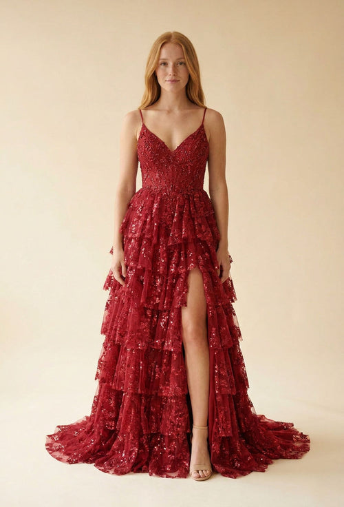 Femme portant une robe de bal rouge à fines bretelles, bustier en dentelle scintillante et jupe à étages froncés à paillettes avec fente haute.