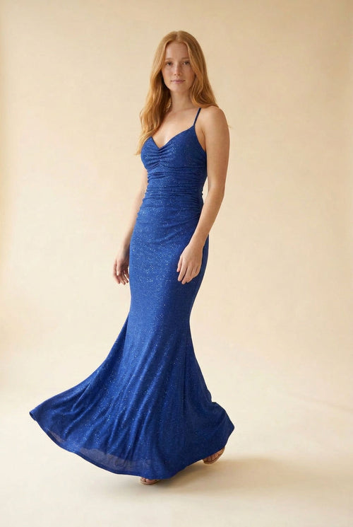 Femme portant une robe sirène bleu royal satinée au décolleté en cœur, bustier drapé froncé et traîne, devant des parois rocheuses.