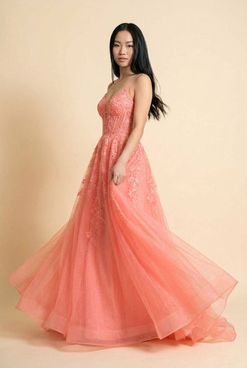 Femme portant une robe de bal corail à bustier corset en dentelle florale et jupe de tulle ample, vue de face.