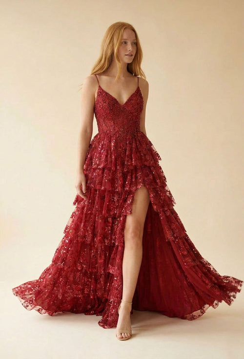 Femme portant une robe de bal rouge à fines bretelles, bustier en dentelle scintillante et jupe à étages froncés à paillettes avec fente haute.