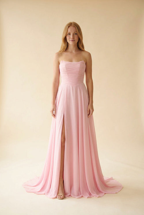 Femme portant une robe de bal rose à bustier droit drapé, jupe de mousseline évasée et fente haute, vue de face.