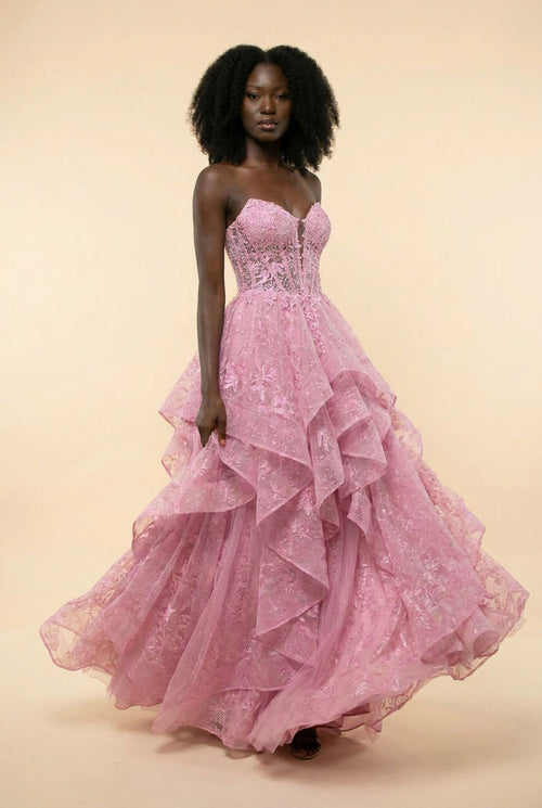 Femme portant une robe de bal rose à bustier cœur en dentelle et jupe de tulle à volants étagés, devant la mer.