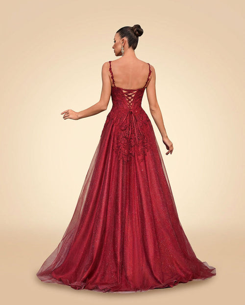 Robe de bal bourgogne à bustier de dentelle florale, décolleté cœur et jupe de tulle scintillant, portée devant une paroi rocheuse noire.