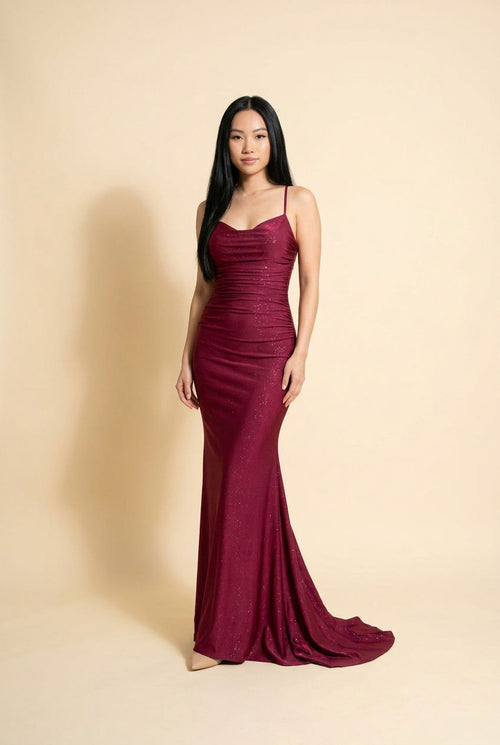 Femme portant une robe de bal sirène à fines bretelles, bustier froncé et décolleté en cœur, avec traîne, photographiée devant des rochers rouges.