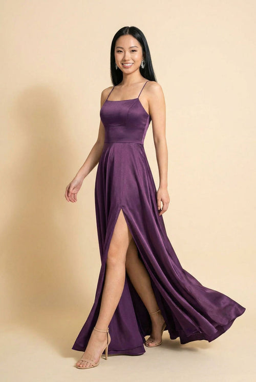 Femme portant une robe de bal en satin prune à encolure droite, bretelles fines, jupe évasée avec fente haute et traîne.
