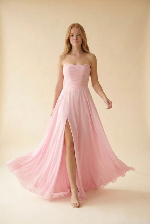 Femme portant une robe de bal rose à bustier droit drapé, jupe de mousseline évasée et fente haute, vue de face.