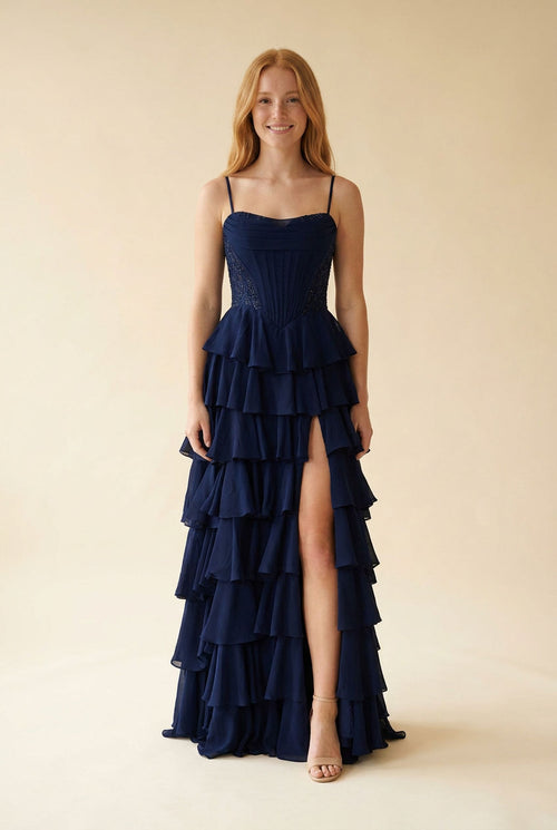 Robe de bal bleu marine à fines bretelles, bustier structuré et jupe de mousseline à volants étagés avec fente sur le devant.